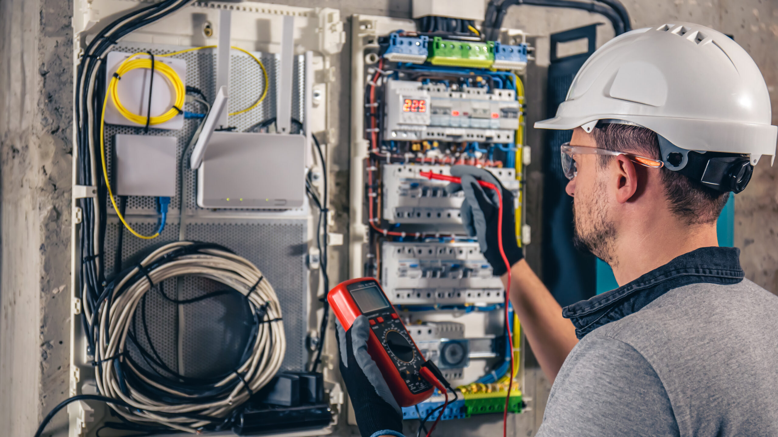 Man, an electrical technician working in a switchboard with fuses. Installation and connection of electrical equipment. Professional uses a tablet.