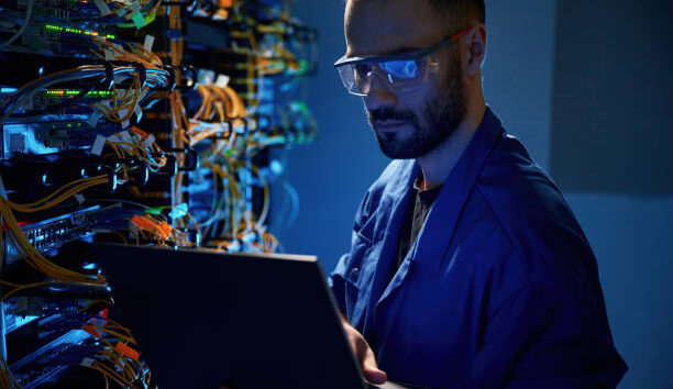 In glasses. Young man is working with internet equipment and wires in server room.